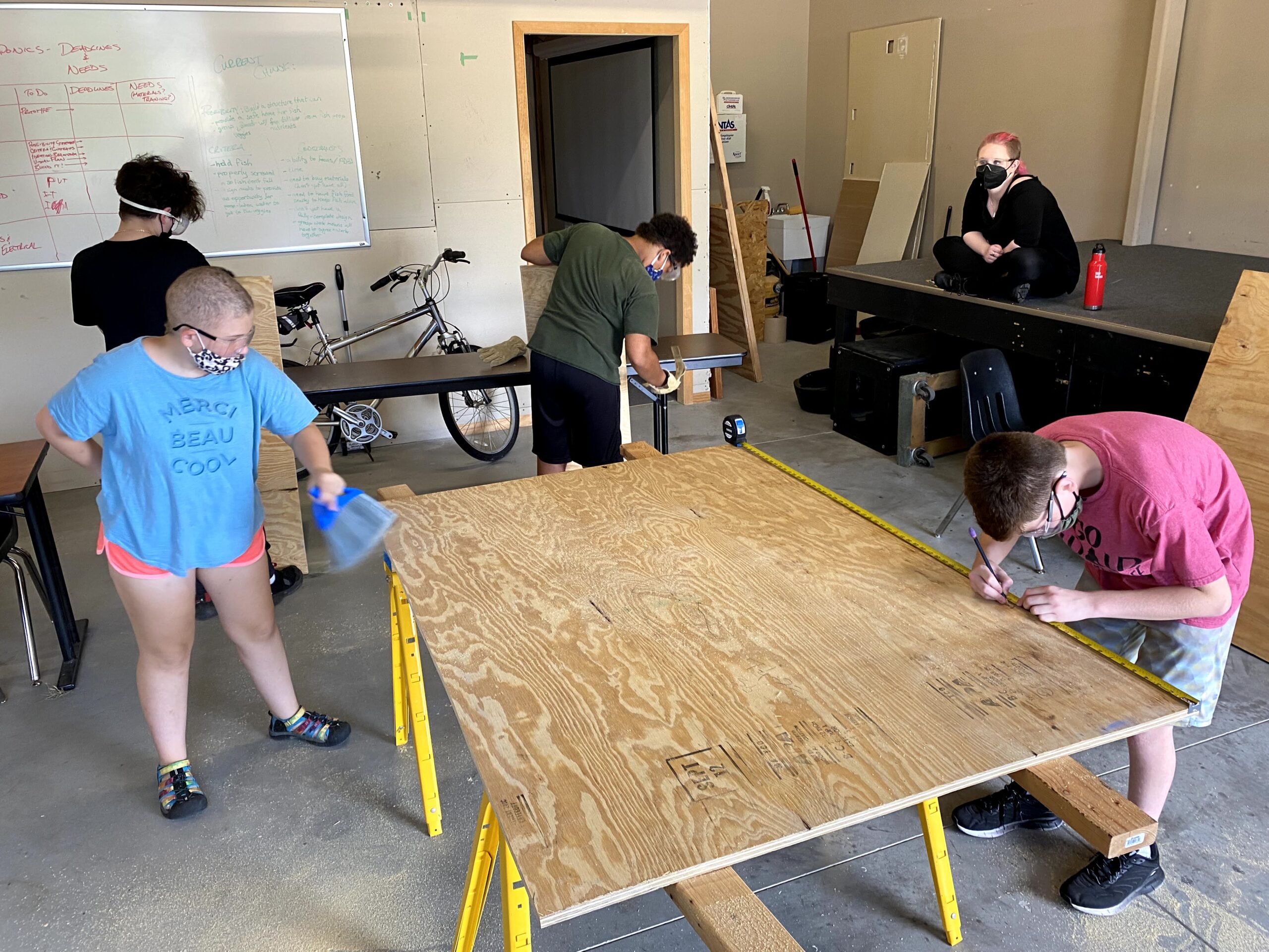 Students in the maker space measuring a sheet of plywood.