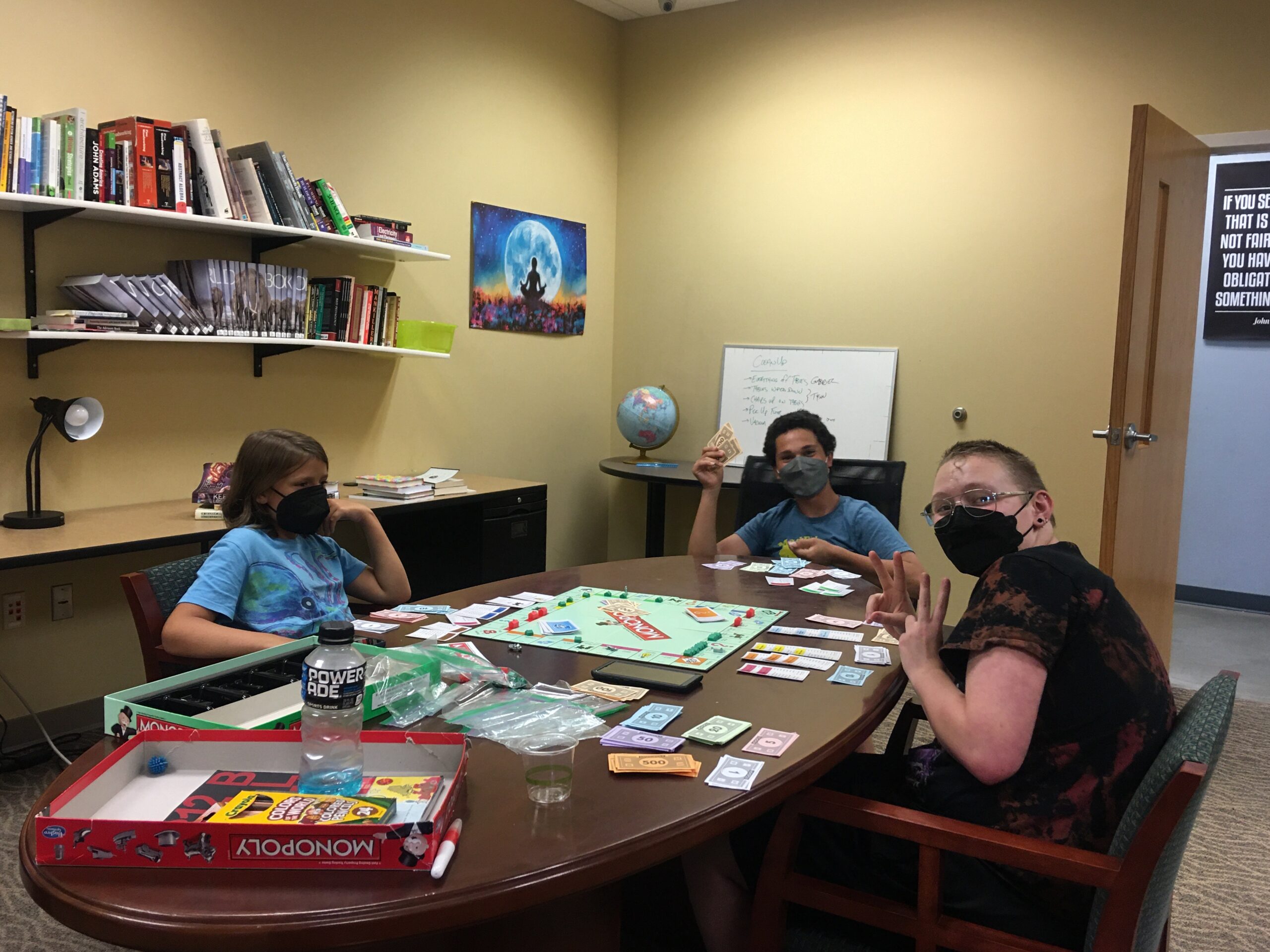 Three students sitting at a table with board games for a club meeting.