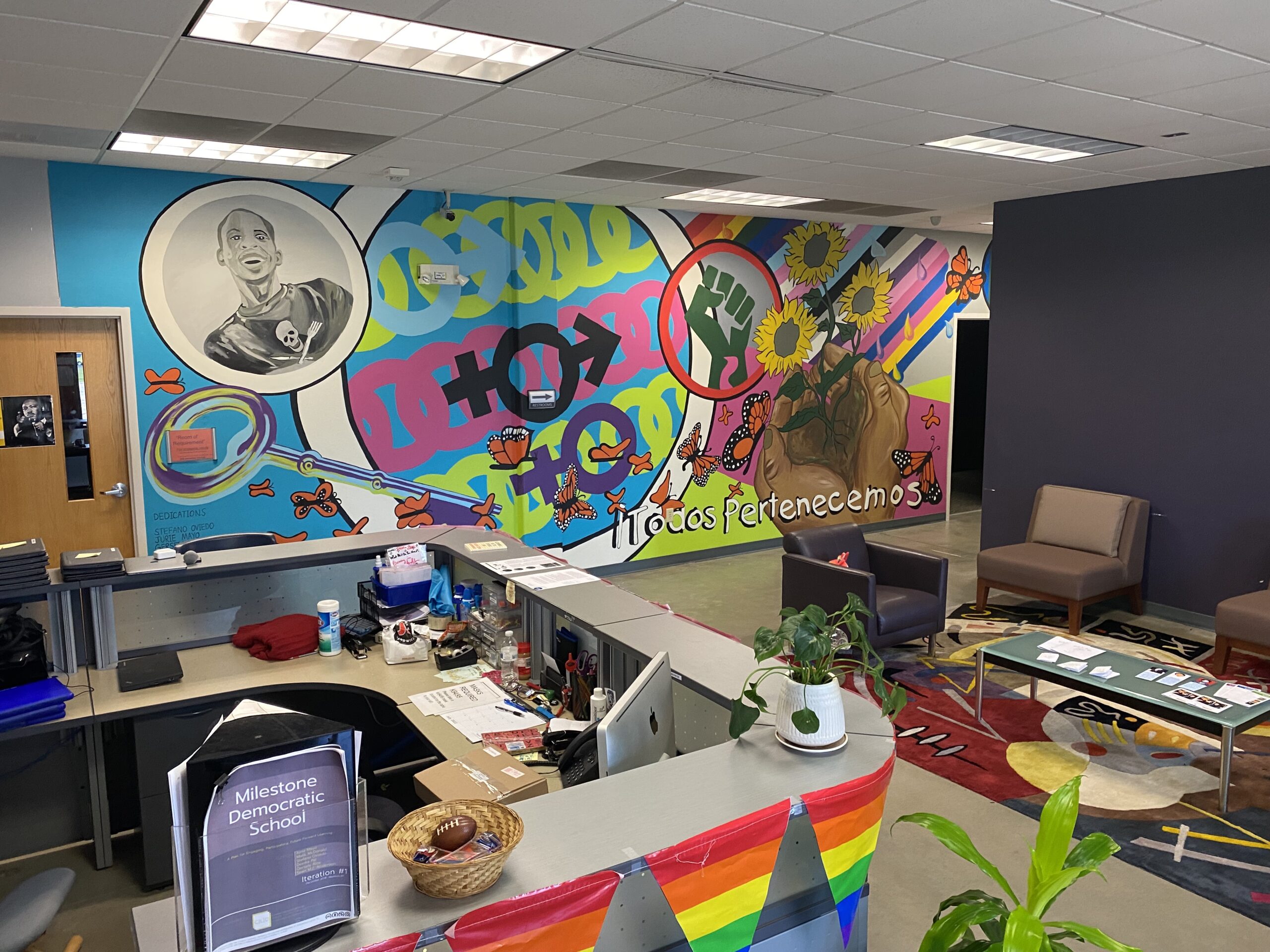 School lobby with bright colored mural and rainbow flags on the desk.